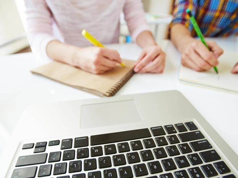 Schüler machen Notizen, vor ihnen liegt ein Laptop