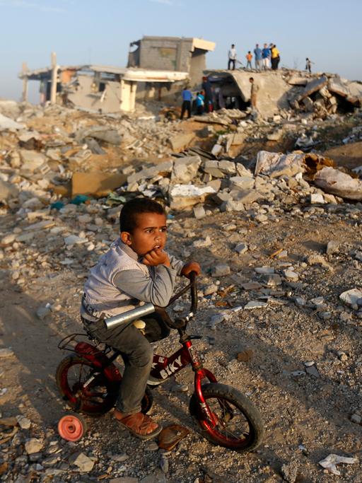 Ein Junge sitzt auf seinem Fahrrad im Gazastreifen inmitten von zerstörten Gebäuden.