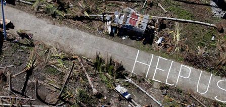 Die Wörter "Help uns" ("Helft uns") sind auf eine freigeräumte Straßen inmitten zerstörter Felder und Häuser gemalt. Die Bewohner der Provinz Leyte auf den Philippinen machen damit auf ihre Not aufmerksam. Das Bild ist aus der Vogelperspektive aufgenommen.