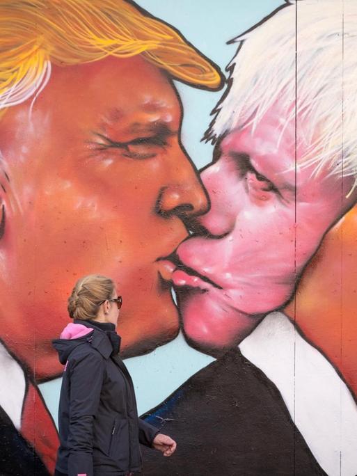Frau geht an einem Wandbild vorbei, das auf ein verfallenes Gebäude in Stokes Croft gemalt wurde und den hoffnungsvollen US-Präsidenten Donald Trump zeigt, der am 24. Mai 2016 in Bristol, England, einen Kuss mit dem ehemaligen Londoner Bürgermeister Boris Johnson teilt