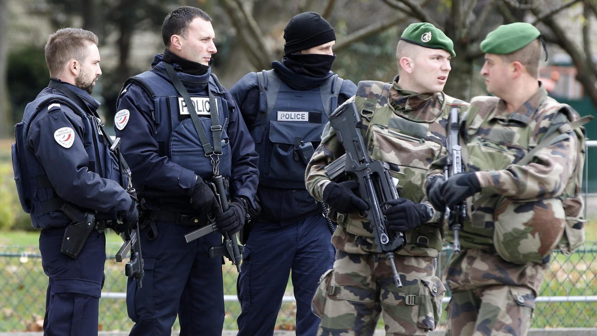 Drei Polizisten in blauer und zwei Soldaten in olivgrüner Uniform stehen zusammen.