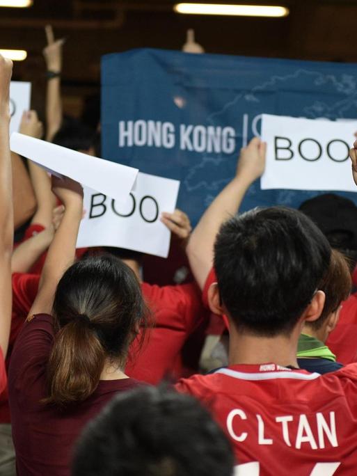 Fußballfans drehen dem Spiel zwischen Iran und Hongkong den Rücken zu und halten Schilder hoch, auf denen "Boo" steht.