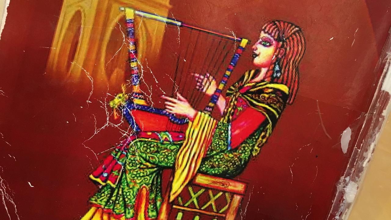 Der abgegriffene Einband des Gesangbuches des syrisch-katholischen Chors "Sonne der Aramäer" in Köln. Das Bild zeigt eine Frau in traditionellem Gewand, die Harfe spielt. 