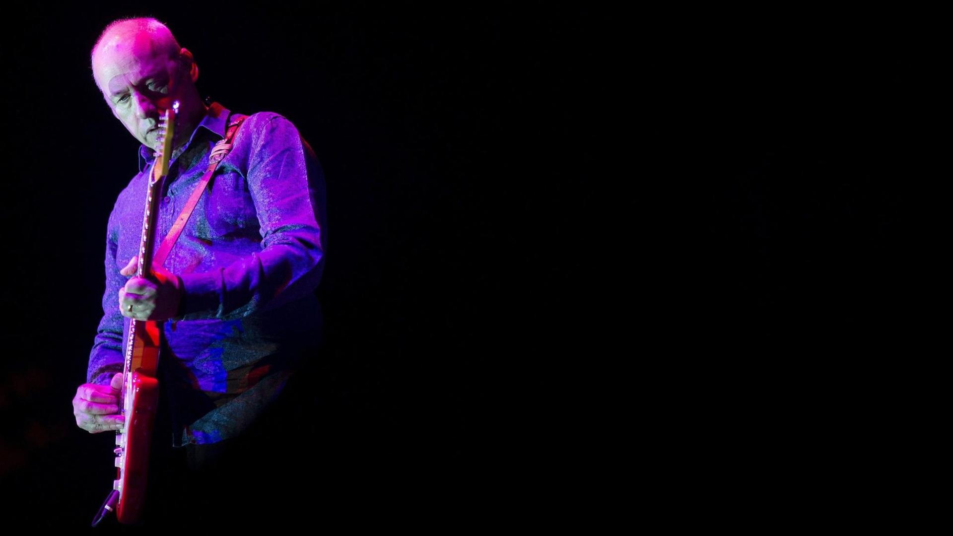 Der Sänger, Gitarrist und Songschreiber Mark Knopfler steht violett-pink angestrahlt während eines Konzerts im spanischen Malaga auf der Bühne.
