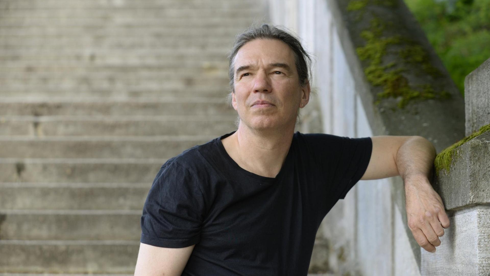 Ein Porträtfoto zeigt Michael Wildenhain, Autor und Schriftsteller angelehnt an eine Treppe im öffentlichen Raum.