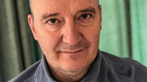 Porträt von Thomas Brussig in grau-blauem Rollkragenpullover vor grünem Hintergrund.