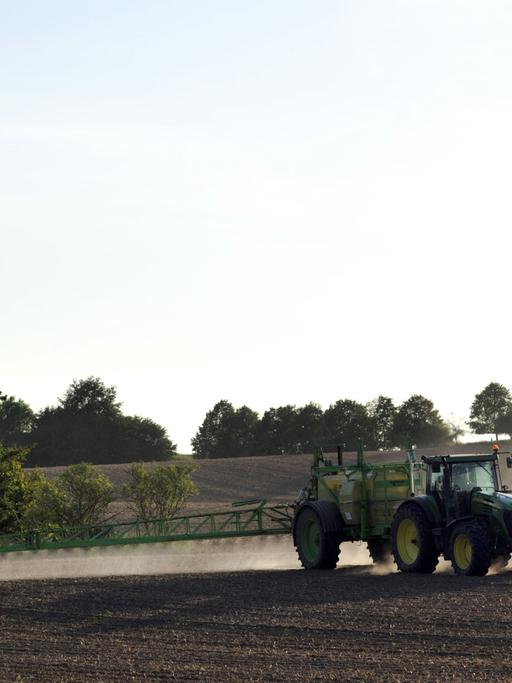 Ein Bauer besprüht mit einem Traktor sein Feld, im Hintergrund ist eine Mühle zu sehen.