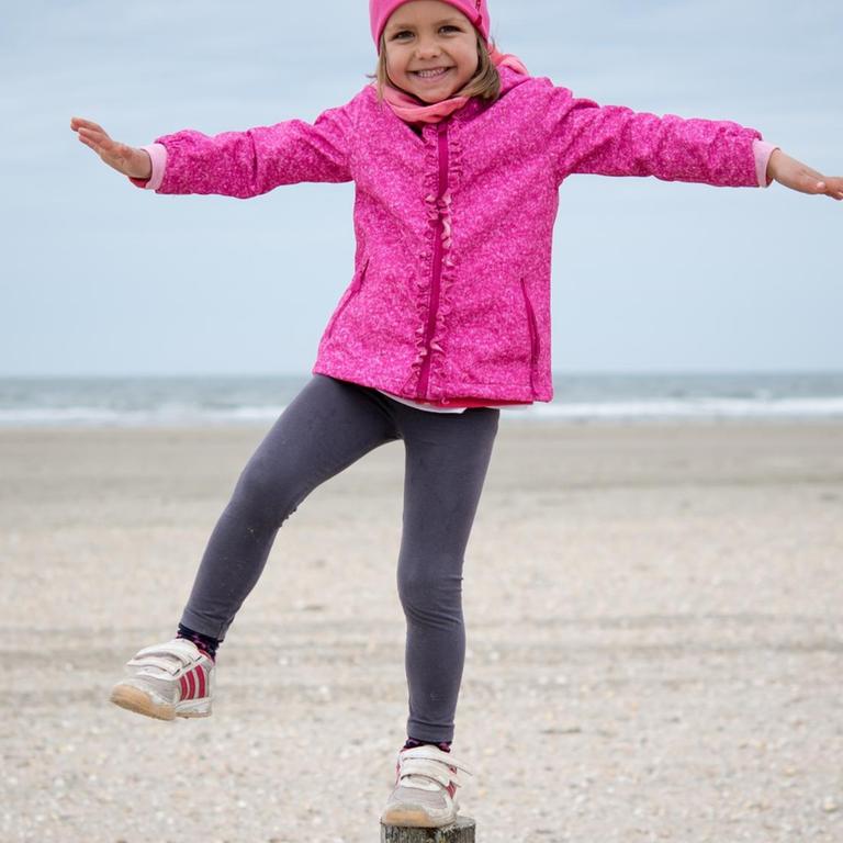 Ein vierjähriges Mädchen beim Balancieren auf einem Holzpfosten am Strand der dänischen Insel Römö.
