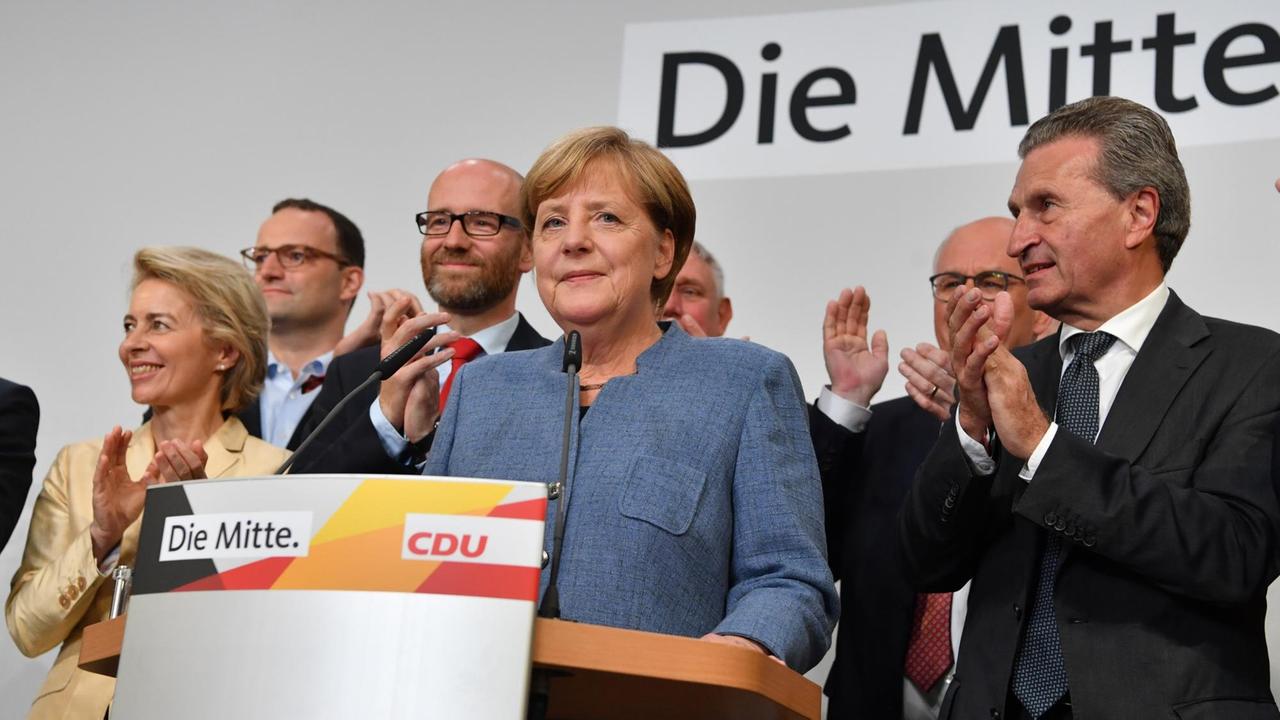 Bundeskanzlerin Angela Merkel (CDU) steht in der Parteizentrale der CDU auf der Bühne. Neben und hinter ihr stehen führende Politiker ihrer Partei und klatschen.