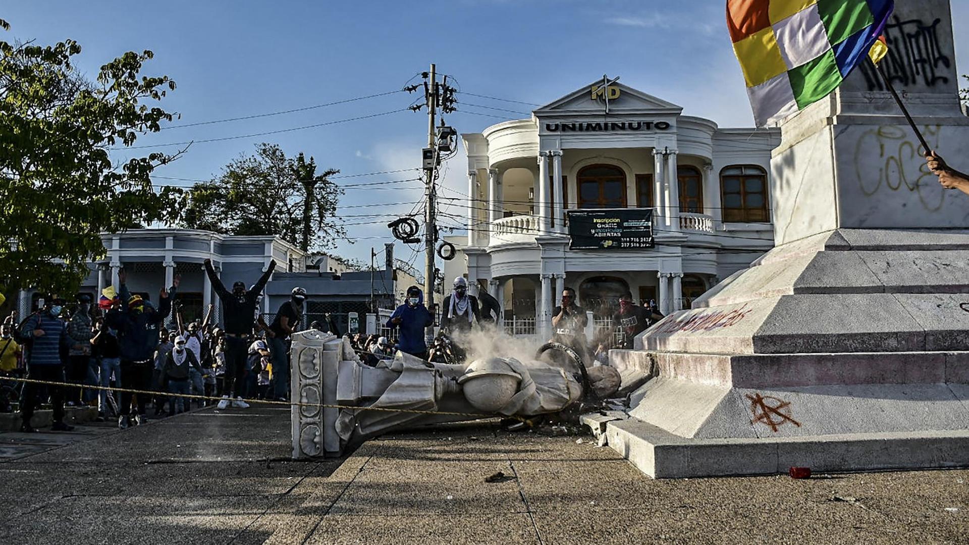 Demonstranten stehen jubelnd neben einer gestürzten Kolumbus-Statur im kolumbianischen Barranquilla.