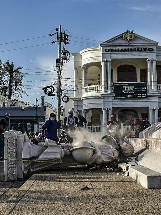 Demonstranten stehen jubelnd neben einer gestürzten Kolumbus-Statur im kolumbianischen Barranquilla.