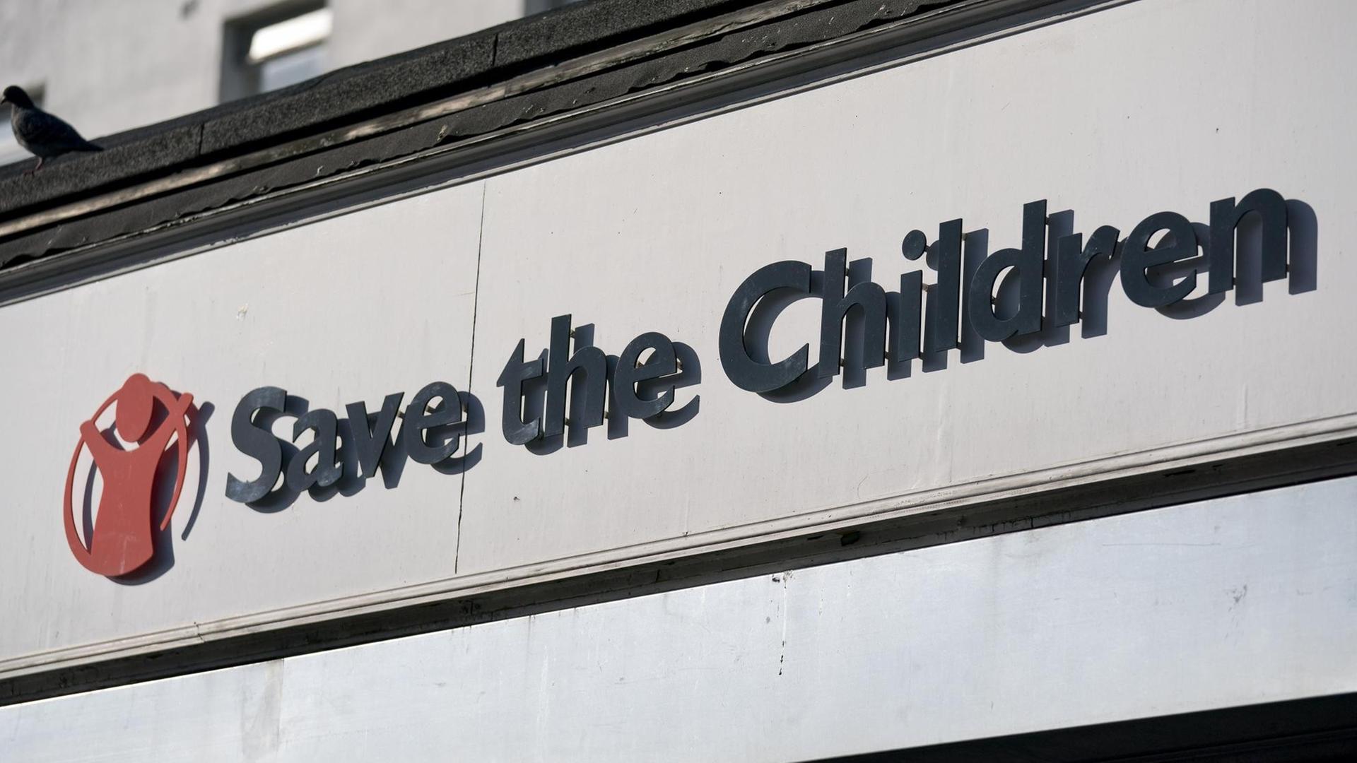 Die Worte "Save the Children" neben einer roten menschenähnlichen Silhouette hängen an einer Häuser-Fassade.