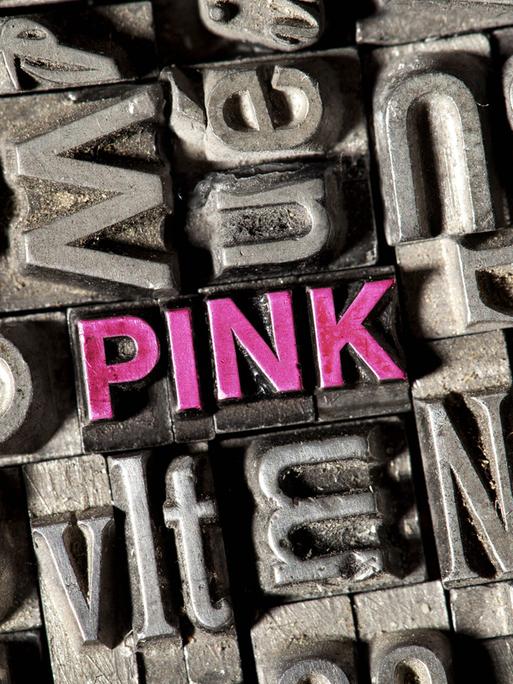 Setzkasten mit Bleilettern, darunter die Buchstaben des Wortes "pink" in rosa