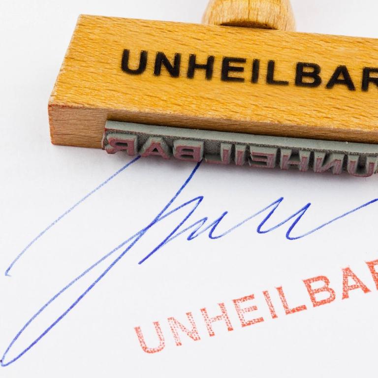 Ein Stempel aus Holz liegt auf einem Dokument - deutsche Aufschrift: "unheilbar"
