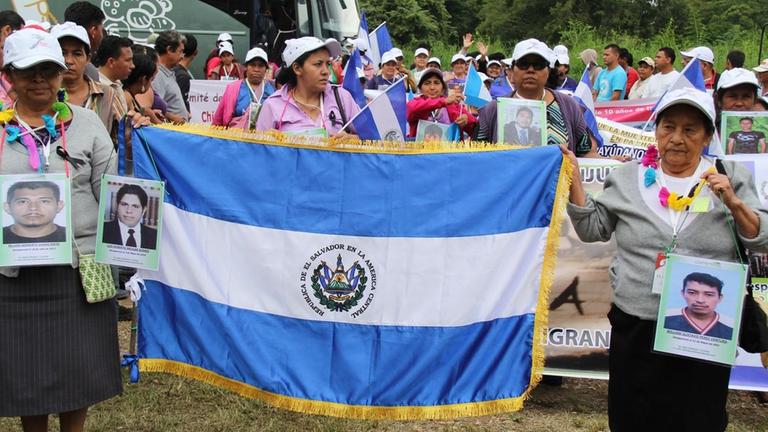 Mehrere Frauen halten Porträts von Männern und die Flagge von El Salvador hoch.