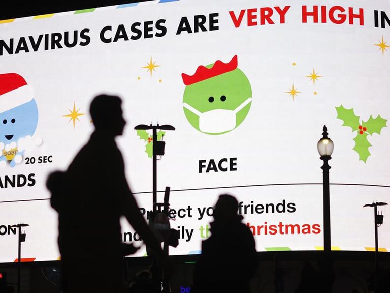 Fußgänger in London laufen an einer digitalen Anzeigentafel vorbei, auf der "Coronavirus-Fälle in London sehr hoch" steht