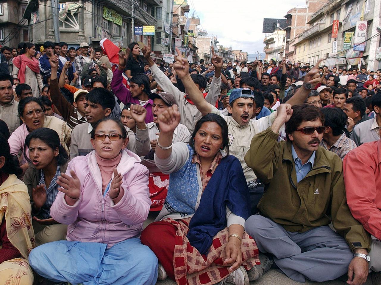Eine große Menschenmasse sitzt auf einer Straße auf dem Boden, reckt Fäuste in die Luft und ruft Parolen.