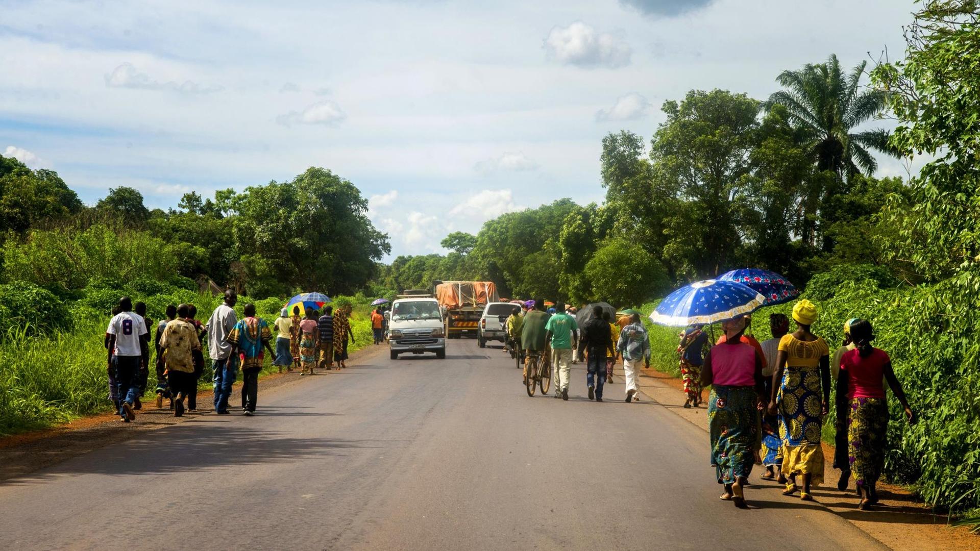 An den Seiten einer Straße im Kongo wandern Menschen entlang, um an ihr Ziel zu kommen.