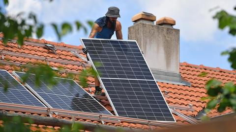 Solarmodule werden auf ein Hausdach transportiert. Ein Arbeiter traegt ein Solarpanel,Solarmodul auf ein Dach eines Wohnhauses. Solarstrom,Solarenergie *** Solar modules are transported on the roof of a house A worker carries a solar panel,solar module on the roof of a house Solar power,solar energy