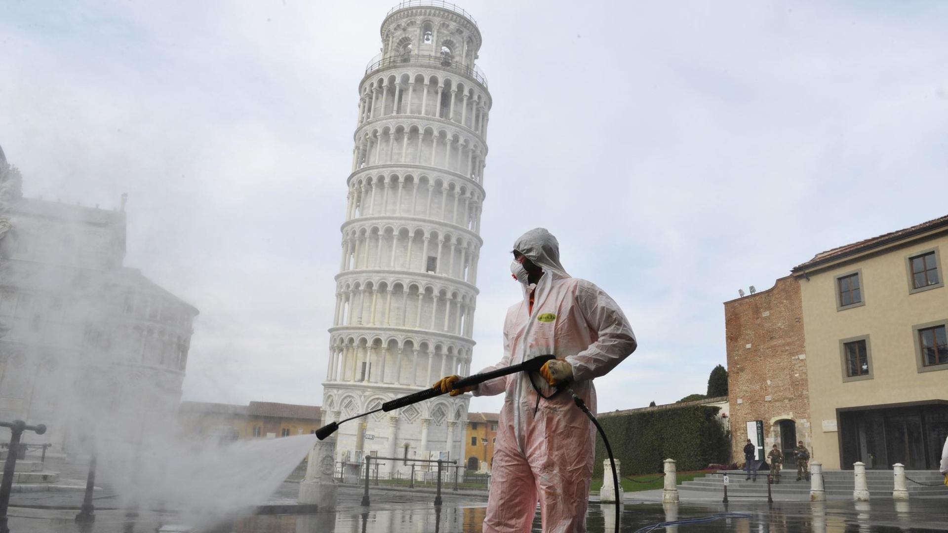 Ein Arbeiter in kompletter Schutzkleidung führt am 17. März 2020 in Pisa auf der Piazza dei Miracoli sanitäre Maßnahmen für den Coronavirus-Notfall durch. Im Hintergrund ist der bekannte schiefe Turm von Pisa zu sehen.