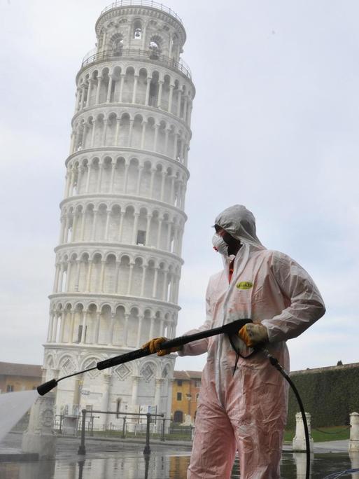 Ein Arbeiter in kompletter Schutzkleidung führt am 17. März 2020 in Pisa auf der Piazza dei Miracoli sanitäre Maßnahmen für den Coronavirus-Notfall durch. Im Hintergrund ist der bekannte schiefe Turm von Pisa zu sehen.