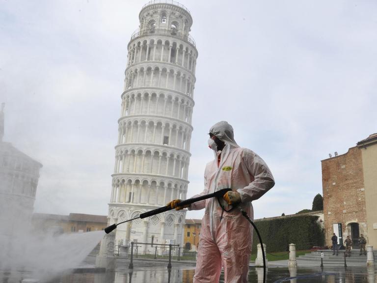Ein Arbeiter in kompletter Schutzkleidung führt am 17. März 2020 in Pisa auf der Piazza dei Miracoli sanitäre Maßnahmen für den Coronavirus-Notfall durch. Im Hintergrund ist der bekannte schiefe Turm von Pisa zu sehen.