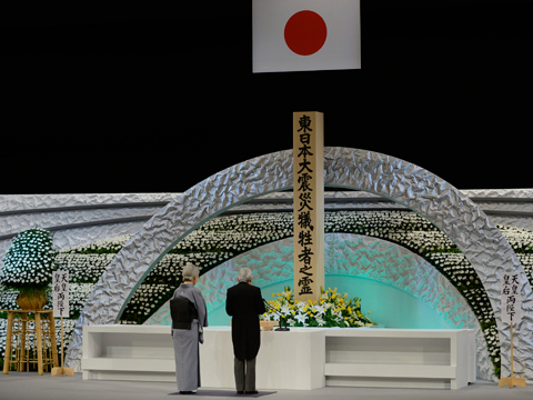 Das japanische Kaiserpaar Akihito und Michiko steht vor einer mit Blumen geschmückten Säule und gedenkt der Opfer der Dreifachkatastrophe von 2011.