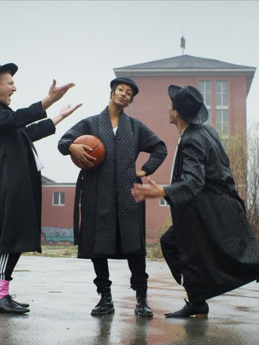 Die Bandmitglieder inszenieren sich auf einem Basketballplatz. Alle tragen einen Hut, einige einen Basketball unter dem Arm.