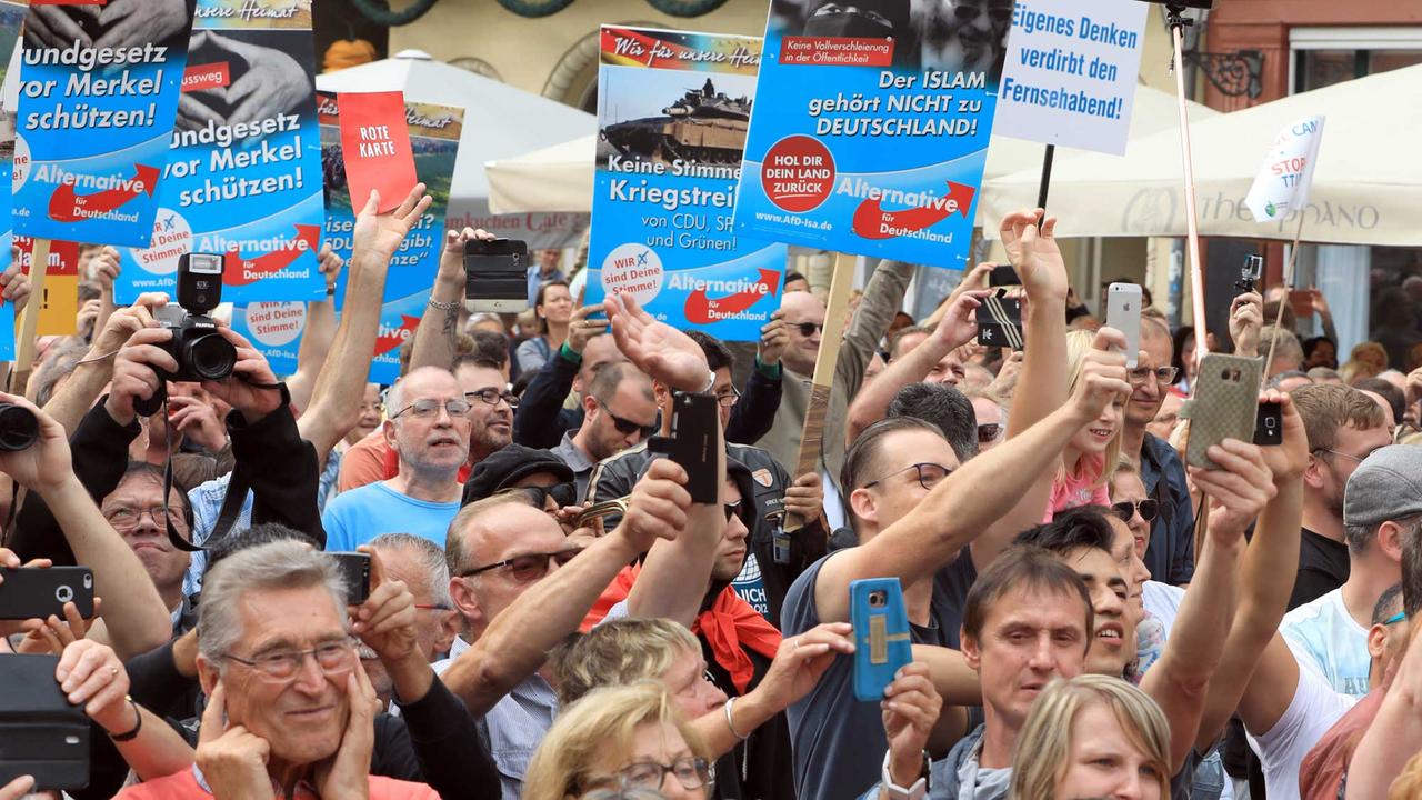 Demonstranten halten am 26.08.2017 am Rande einer Wahlkampfveranstaltung der CDU mit Bundeskanzlerin Merkel auf dem Marktplatz in Quedlinburg (Sachsen-Anhalt) Plakate der Partei Alternative für Deutschland (AfD). 