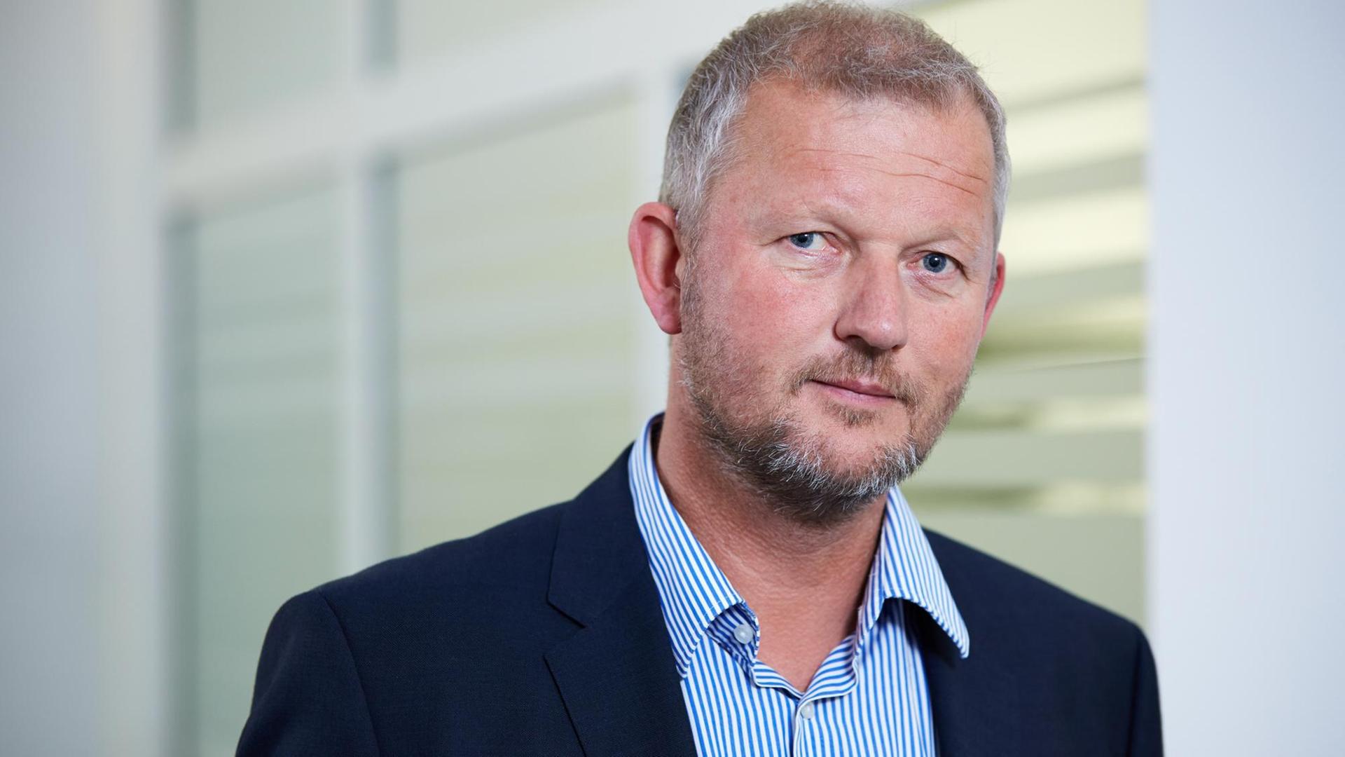 Das Bild zeigt Olaf Köller in einer Nahaufnahme. Er trägt ein Jacket und Hemd mit einem offenen Kragen ohne Krawatte.