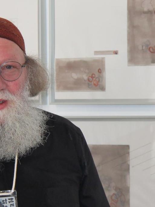 Der Komponist Jakob Ullmann steht in einer Galerie vor seinen bildnerischen Arbeiten