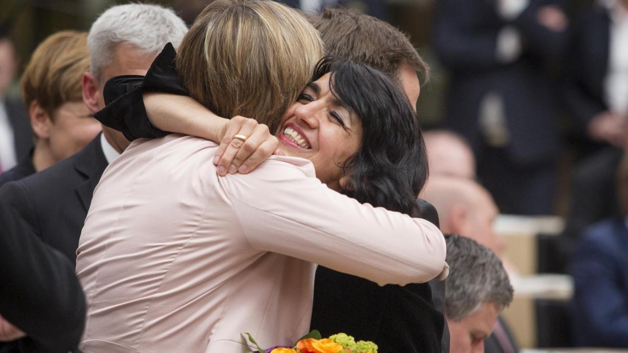 Die beiden Politikerinnen umarmen sich im Plenum; Aras hält einen bunten Blumenstrauß in der Hand.