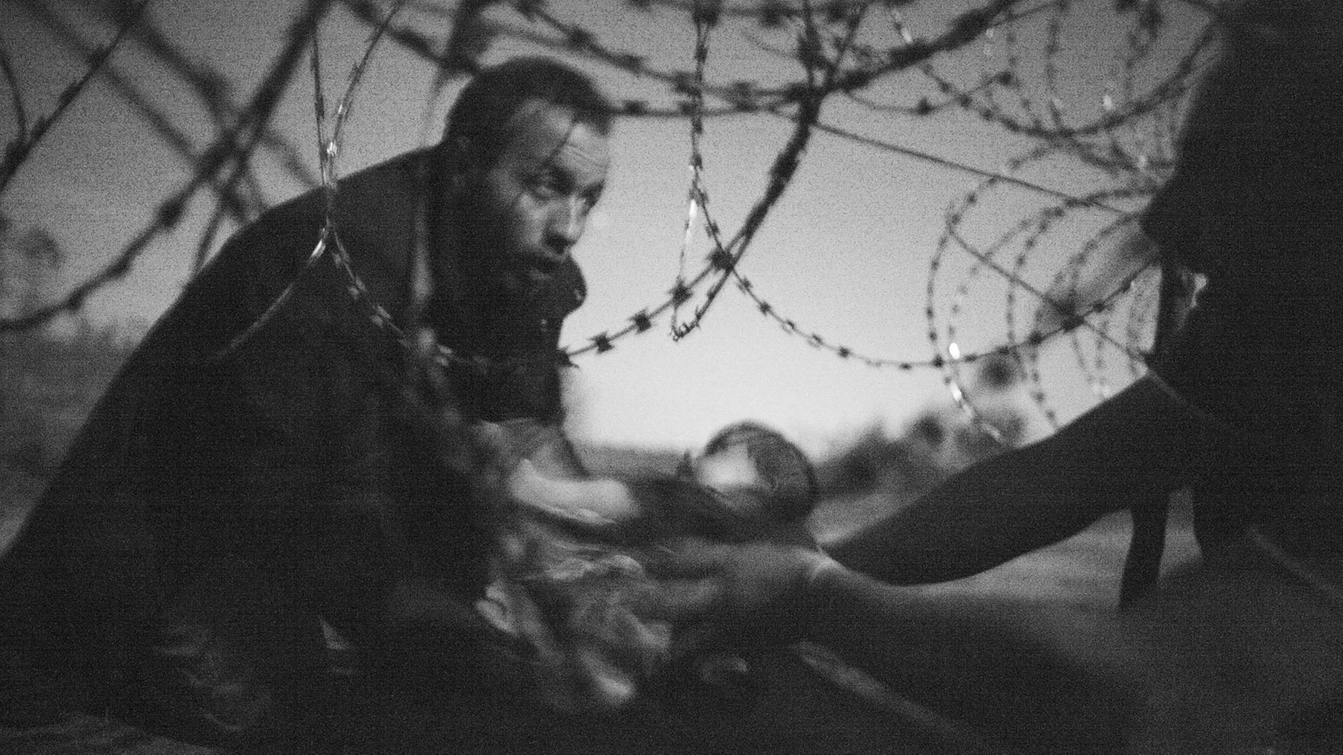 Flüchtlinge reichen ein Baby durch den Stacheldrahtzaun an der serbisch-ungarischen Grenze.