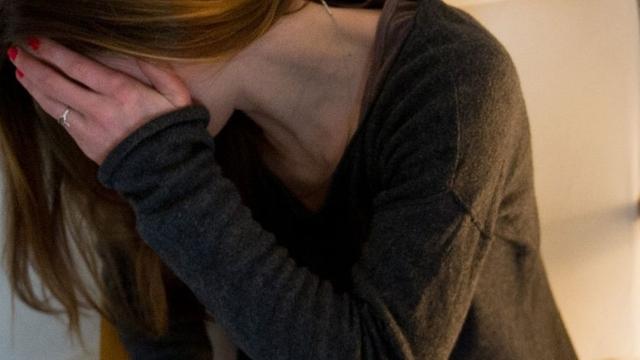 Eine Frau hält sich ängstlich die Hand vor ihr Gesicht.