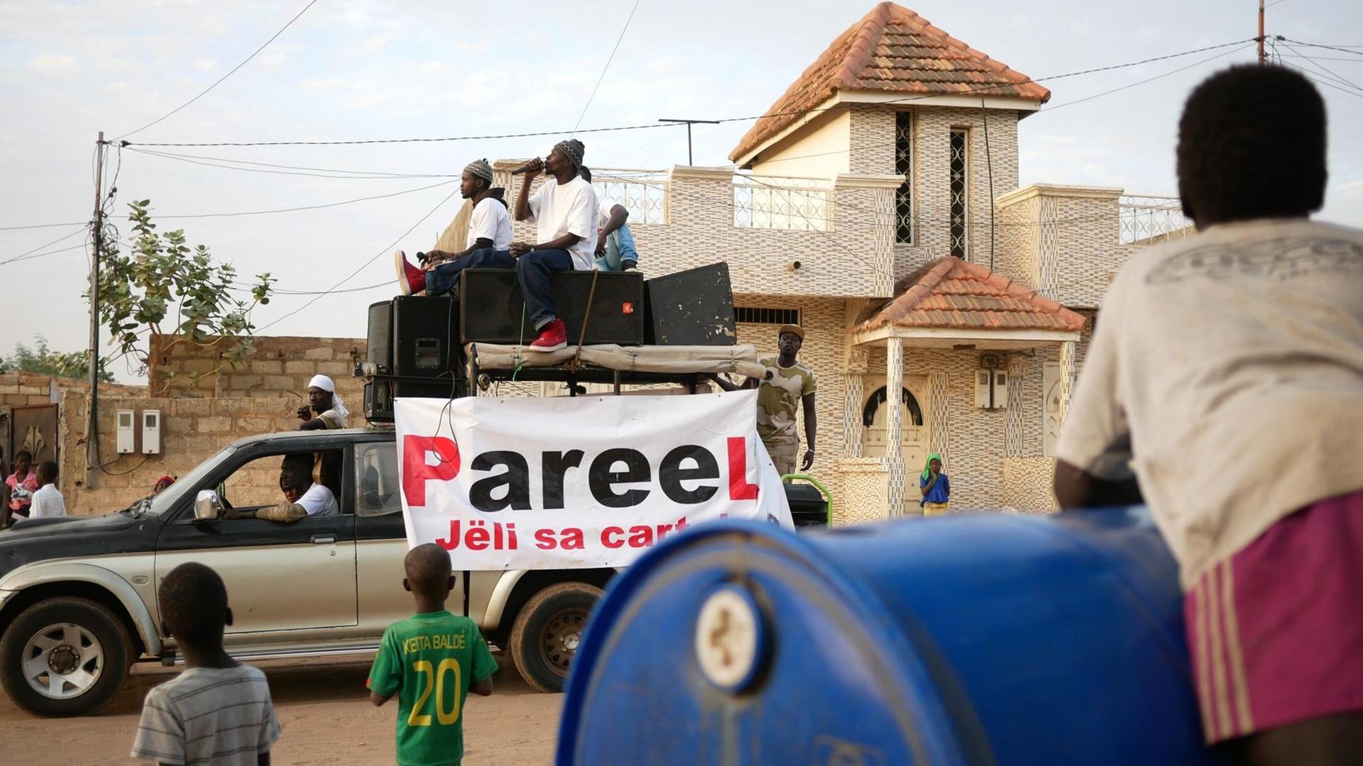Die Rapper der senegalesischen Protestbewegung "Y’en a Marre" – "Wir haben es satt". Sie sitzen auf einem Auto und fahren durch eine staubige Straße.