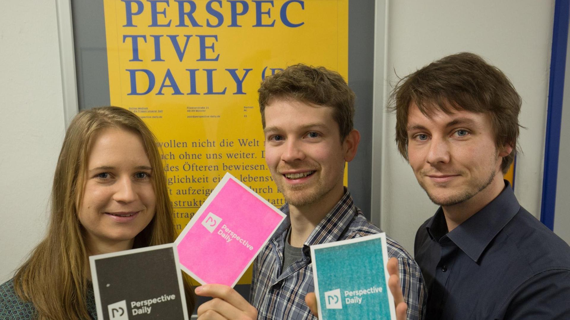Die Medienmacher Maren Urner, Bernhard Eickenberg (r) und Han Langeslag halten am 04.02.2016 in Münster Werbepostkarten mit dem Namen ihres geplanten Online-Magazins «Perspective Daily» vor einem gleichnamigen Werbeplakat in den Händen.
