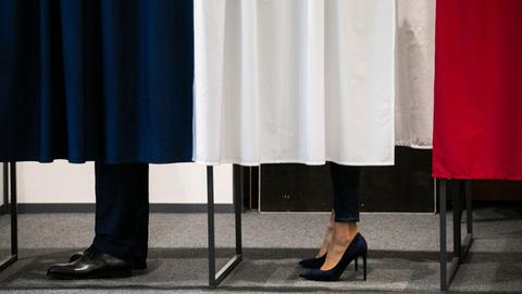 Das Bild zeigt die Füße von Emmanuel und Brigitte Macron in einer Wahlkabine