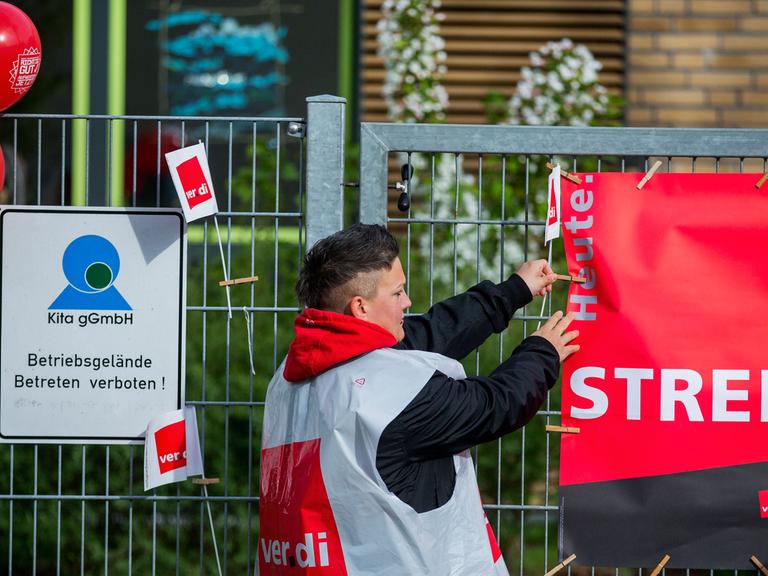 Eine Erzieherin der Kindertagesstätte "Kirschblüte" hängt in Schwerin ein Streik-Plakat an den Eingang der Einrichtung.