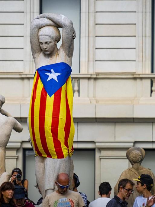 Demonstranten haben eine Frauenstatue auf der Plaxa Catalunya in Barcelona in eine katalonische Flagge eingewickelt.