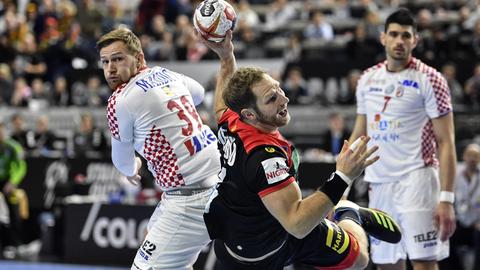 Das Bild zeigt eine Szene aus dem Handball-WM-Hauptrundenspiel Deutschland gegen Kroatien in Köln. Der deutsche Nationalspieler wirft den Ball auf das kroatische Tor und befindet sich dabei nach einem Absprung in der Luft. Gegnerische Spieler schauen ihm dabei zu.