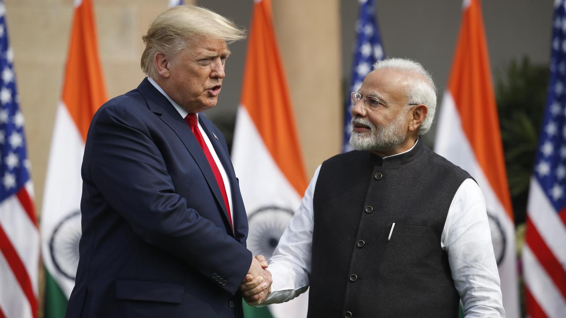 US-Präsident Trump schüttelt dem indischen Premierminister Modi die Hand. Ihnen ihnen die Flaggen der beiden Länder.