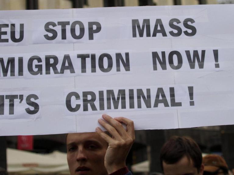 Proteste gegen die EU-Verteilungsquote für Flüchtlinge in Lettlands Hauptstadt Riga. Ein Demonstrant hält ein Schild in die Höhe auf dem steht: "EU stop mass immigration now. It's criminal!" (Auf Deutsch: "EU beende die Masseneinwanderung jetzt. Das ist kriminell!")