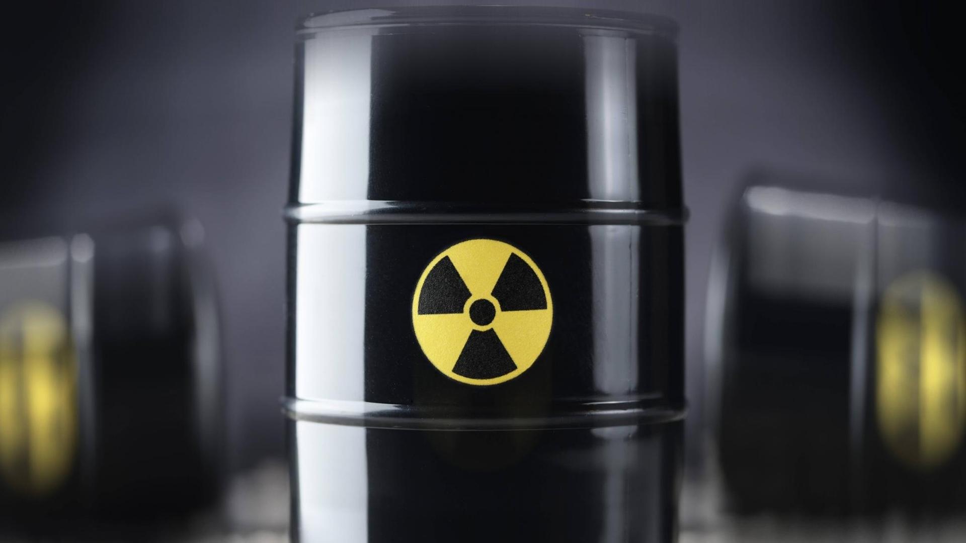 Drei schwarze Atommüll-Fässer, wobei eines im Vordergrund in der Mitte scharf abgebildet ist, im Hintergrund zwei weitere Fässer unscharf.