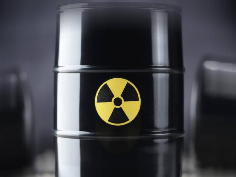 Drei schwarze Atommüll-Fässer, wobei eines im Vordergrund in der Mitte scharf abgebildet ist, im Hintergrund zwei weitere Fässer unscharf.