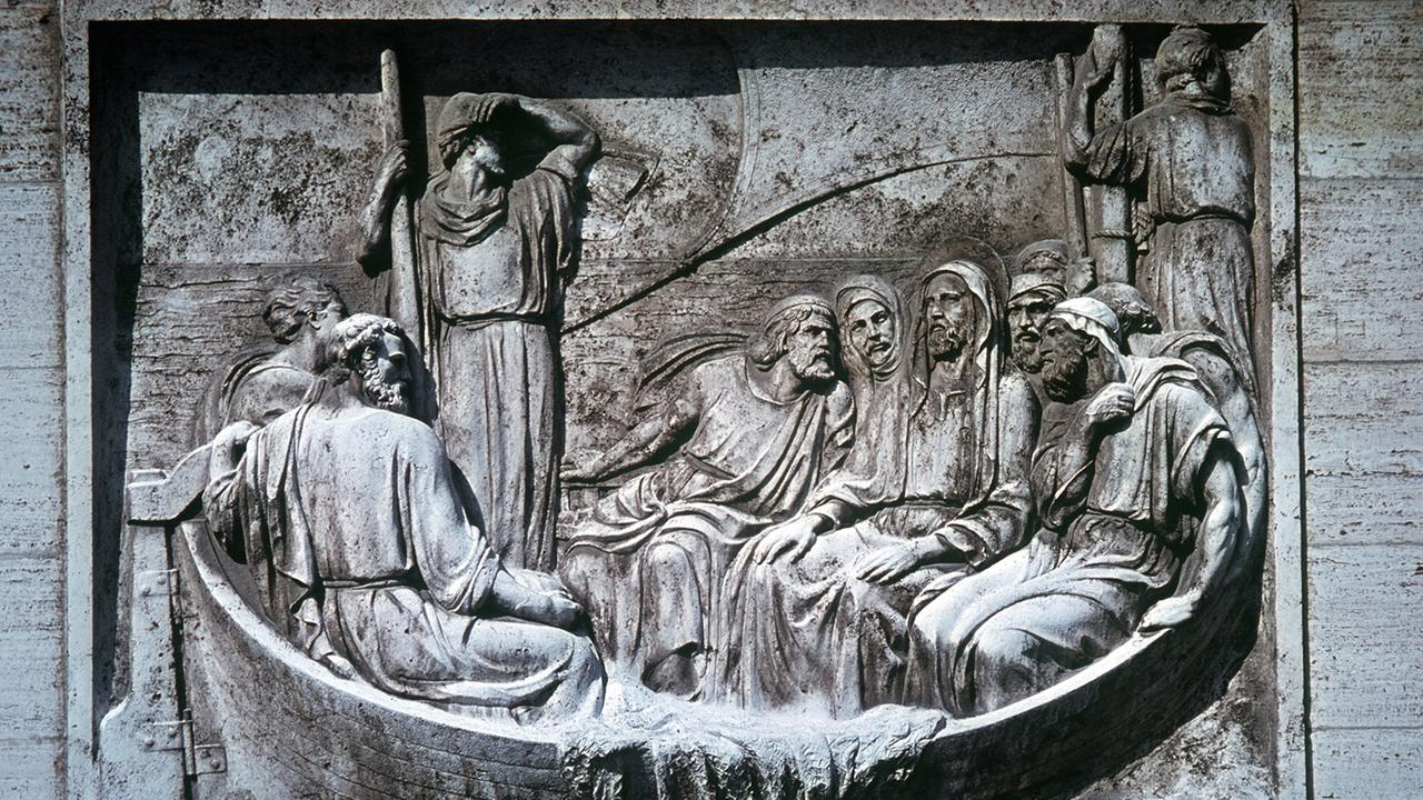 Das Bild zeigt ein Relief am Vatikan-Bahnhof in Rom. Zu sehen ist, wie Jesus und seine Jünger mit einem Boot den See Genezareth befahren.