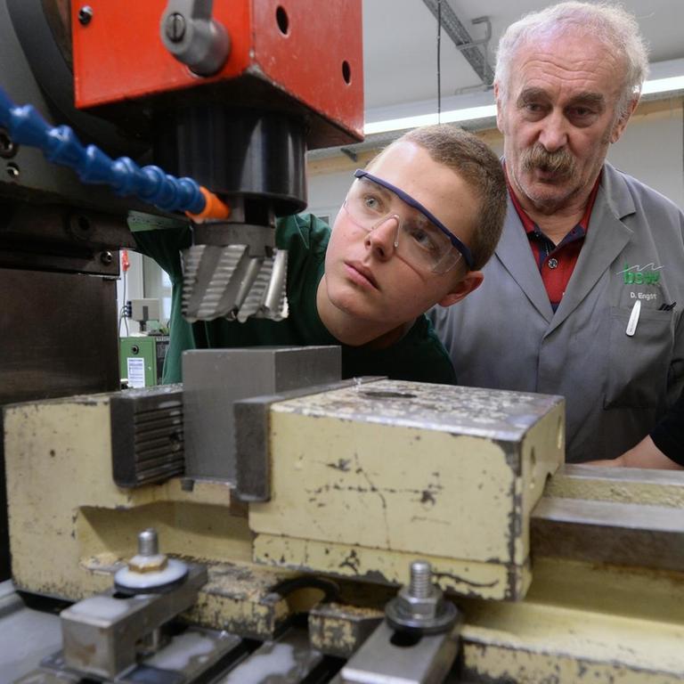 Der Pole Rajmund Boruch und der Bulgare Nikolay Dimitrov beugen sich gemeinsam mit ihrem Ausbilder über eine Maschine in der Metallwerkstatt des Bildungswerks der Sächsischen Wirtschaft.