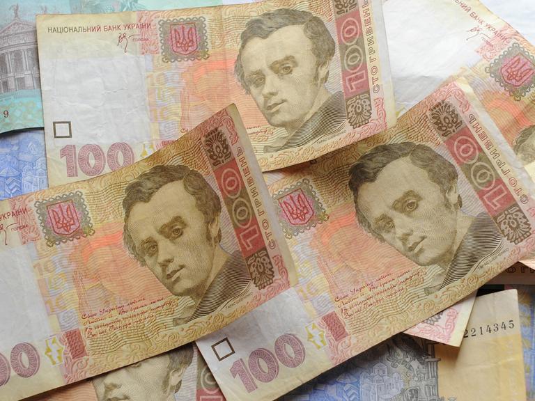 Auf einem Tisch liegen ein Dutzend Geldscheine der ukrainischen Währung Hrywnja, vor allem 1-, 20- und 100-Hrywnja-Scheine.