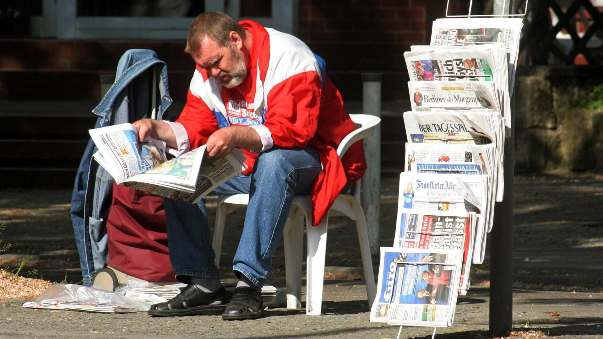 Ein Zeitungsverkäufer liest neben seinem Stand in einer Zeitung