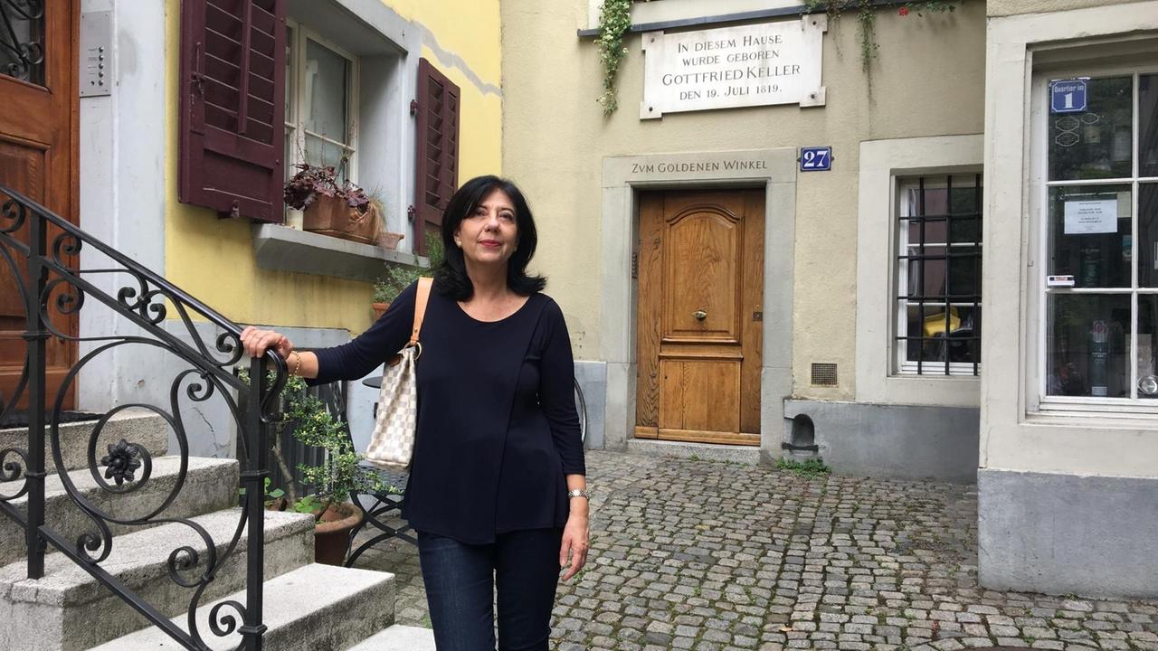 Ursula Amrein steht - die Hand auf einem Treppengeländer - vor dem Geburtshaus von Gottfried Keller. 
