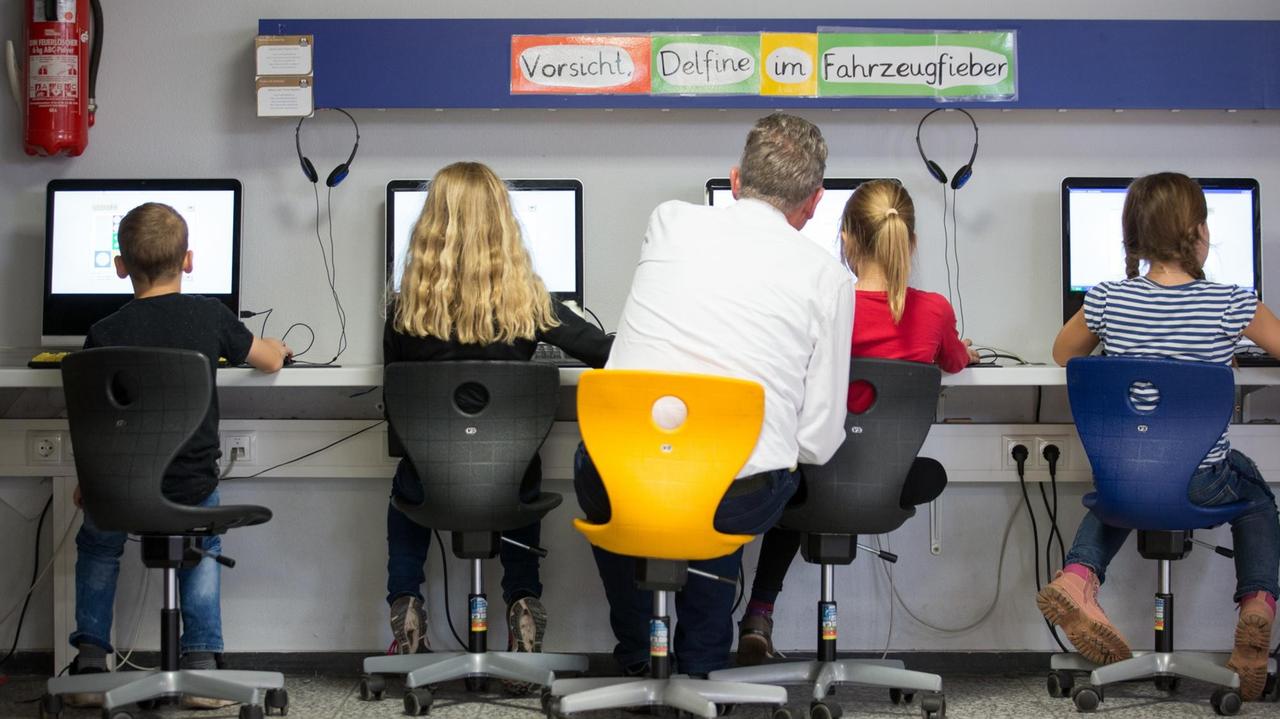Schüler und ihr Lehrer arbeiten in einem Klassenraum einer Grundschule an Computern.